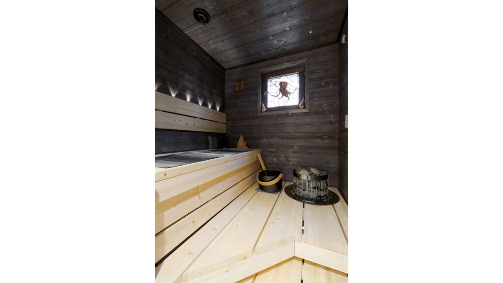 Tumma sauna, jossa vaaleat lauteet, LED-spottivalot ja lasimaalausikkuna.