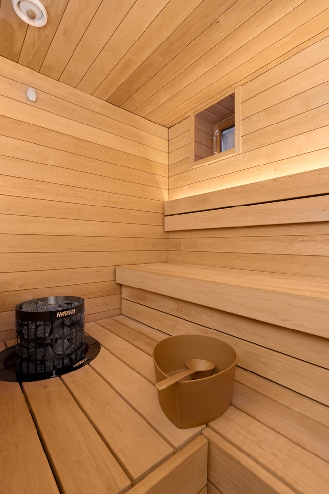 Pieni vaalea sauna – L-malliset kulmalauteet, LED-nauhavalaistus ja Harvia-häkkikiuas.