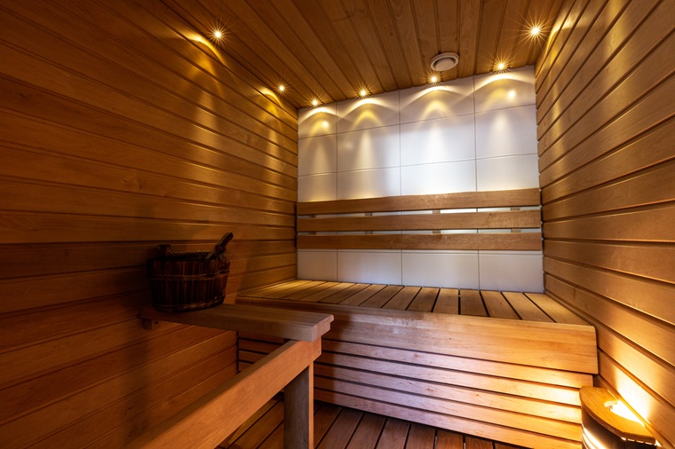 Lämminsävyinen puinen sauna, jossa valkoinen laattaseinä ja LED-spottivalot.