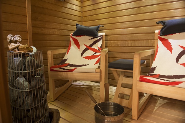 Lämminsävyinen puinen sauna – kaksi saunatuolia värikkäillä lehtikuvioisilla päällisillä.