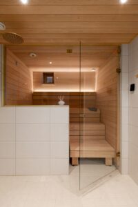 Vaalea sauna – lasiseinä, kultaiset yksityiskohdat ja porraslauteet.