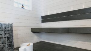 Valkoinen sauna vaakapaneelilla – tummat kelluvat kulmalauteet ja häkkikiuas.