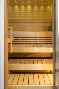 Vaalea puinen sauna – kolme laudetasoa, selkänoja ja LED-valot.